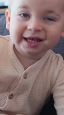 Evdeki kanepede gülen beyaz bir çocuğun portresi. Keyif, çocukluk ve iyi ruh hali kavramı. Dikey video.