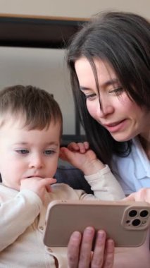 Küçük çocuk ve pozitif anne cep telefonuyla çizgi film izliyor, evdeki kanepede dinleniyor. Dikey video.