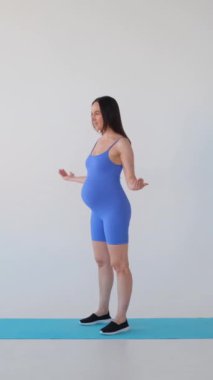 Beyaz arka planda spor yapan orta yaşlı, hamile, beyaz kadın sporcu. Hamilelik ve egzersiz konsepti. Dikey video.