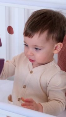 Meraklı beyaz çocuk tahta oyuncaklarla oynuyor, beşikte yatak odasında oturuyor. Hayal gücü ve eğlence kavramı. Dikey video.