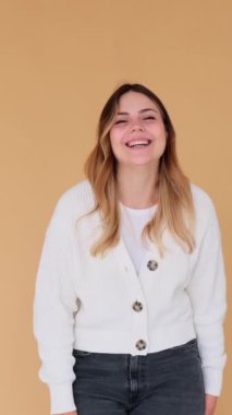 Memnun ve arkadaş canlısı beyaz kadın gülüyor, bej arka planda duruyor. Keyif ve kahkaha konsepti. Dikey video.