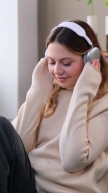 Huzurlu Kafkasyalı genç kadın evde dinleniyor ve kulaklıkla müzik dinliyor, ev içi boş zaman geçiriyor. Dikey video.