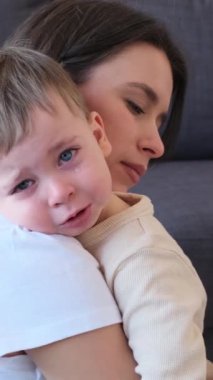 Evdeki sevgili annesinin omzunda ağlayan, küçük beyaz bir çocuk. Çocuk gözyaşı ve keder kavramı. Dikey video.