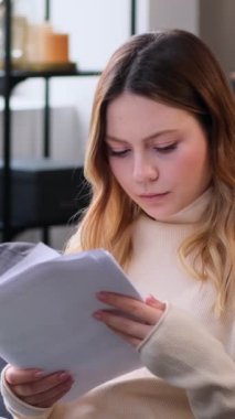 Evraklarla çalışan, bütçeyi planlayan oturma odasındaki kanepede oturan, ciddi, genç, beyaz bir kadın. Dikey video.