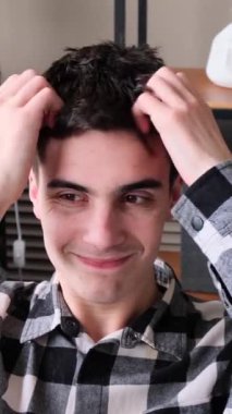 Kafası kaşınan ve evinde kaşınan genç, yetişkin, beyaz bir adam. Deri hastalığı, alerji ya da deri iltihabı. Dikey video.