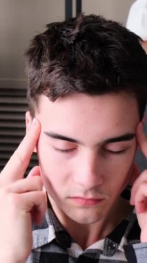 Evdeki kanepede oturan, baş ağrısı ya da hastalıktan muzdarip üzgün, beyaz, genç bir adam. Baskı ve stres kavramı. Dikey video.