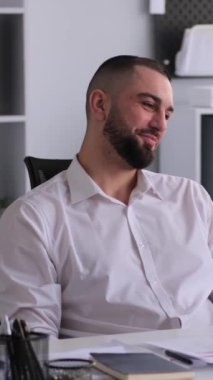 Kafkasyalı, dost canlısı, orta yaşlı bir işadamı ofiste çalışırken çevrimiçi video görüşmesine katılmış. Sanal toplantı ve iletişim konsepti. Dikey video.