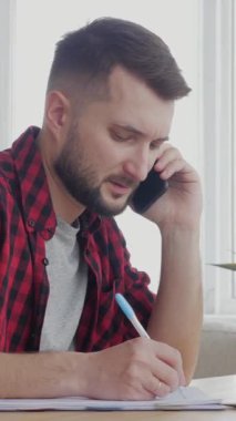 Düşünceli orta yaşlı Kafkas işadamı iş görüşmesi için cep telefonunu ev oturma odasına çağırmış. Dikey video.