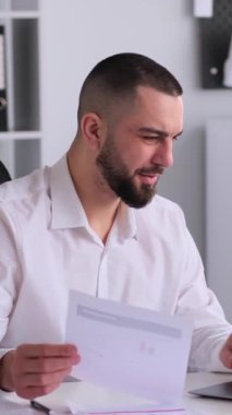 Sırıtkan orta yaşlı beyaz erkek, ofiste laptop ve belgelerle çalışıyor. İş muhasebesi kavramı. Dikey video.