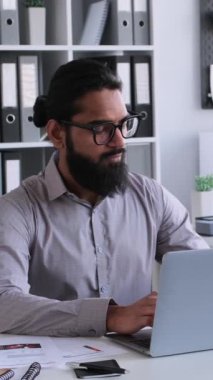 Ofiste laptopla çalışan ve kahve içen dalgın, orta yaşlı bir Arap işadamı. Meşgul bir iş adamı kavramı. Dikey video.