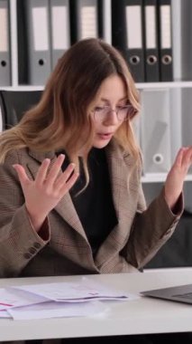 Ofiste çalışırken çevrimiçi video görüşmelerine liderlik eden Kafkas asıllı genç bir bayan. Duygusal stres kavramı. Dikey video.