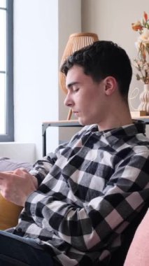 Sosyal medyada cep telefonuyla sosyal medyada mesajlaşan mutlu, genç, beyaz bir adam. Uzaktan iletişim kavramı. Dikey video.