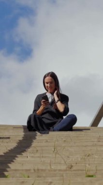 Dışarıda dinlenen bir kadın, doğada barışçıl bir tatil macerası sırasında çevrimiçi mesajlaşma için telefon kullanıyor. Etrafı vahşi yaşamla çevrili sakin bir an. Dikey video.