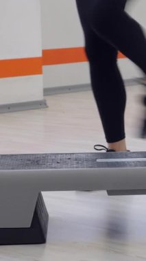 Spor aletleri kullanarak spor antrenmanına katılan beyaz bir genç kadının yakın çekimi ya da adım aerobiği. Dikey video.