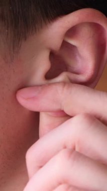 Yakından, genç, beyaz bir adamın kafasının detaylı bir fotoğrafı, kulak ve kulak memesini okşuyor. Vücut parçası kavramı, ilgi ve kulak organı. Dikey video.