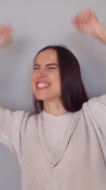 Beyaz arka planda başarıyı kutlamak için orta yaşlı mutlu bir kadın baş parmağını kaldırıyor ya da hareket ve dans ediyor. Dikey video.