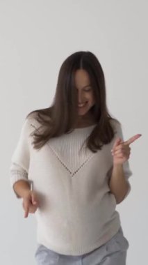 Gülen hamile bir kadın dans ediyor ve beyaz bir arka planda müzik eşliğinde eğleniyor, hamilelik boyunca mutluluk, eğlence ve heyecan ifade ediyor. Dikey video.