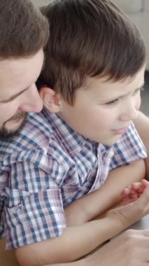 Neşeli orta yaşlı beyaz baba ve oğlu evde dizüstü bilgisayar kullanarak zaman geçiriyorlar. Aile sevgisi kavramı. Dikey video.