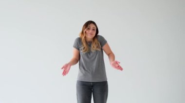 Beyaz arka planda omuz silken, kafası karışmış, beyaz, genç bir kadının portresi. Yanlış anlama, güvensizlik ya da belirsizlik işareti.