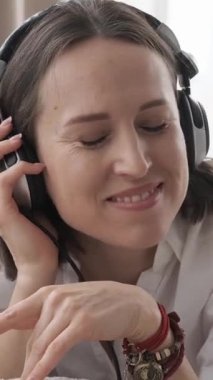 Memnuniyet veren kadın evdeki kanepede dinleniyor, boş zamanlarını müzik dinleyerek geçiriyor. Huzurlu bir atmosferde eğlence, tamamen rahatlatıcı ve keyifli ana dalmış. Dikey video.