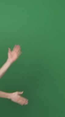 Olumlu, arkadaş canlısı bir kadın yeşil arka planda eğleniyor ve eğleniyor, enerjik hareketlerle mutluluğu ifade ederken kendini rahat ve meşgul hissediyor. Dikey video.