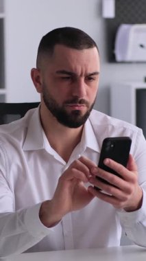 Ofiste çalışan düşünceli bir işadamı cep telefonu kullanıyor, mali durumları analiz ediyor ve iş muhasebeleriyle ilgileniyor. Dikey video.