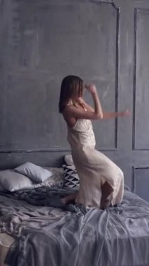 Neşeli bir kadın yatakta dans ediyor ve ev partisinde eğleniyor, bayramı neşe, eğlence ve şenlik havasıyla kutluyor. Dikey video.