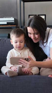 Mutlu Kafkasyalı genç anne ve küçük oğlu cep telefonlarını evde eğlenmek için kullanıyor. Dijital eğlence konsepti. Dikey video.