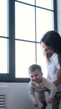 Evde vakit geçirirken oyun oynayan heyecanlı, genç, beyaz bir anne ve bebek. Mutlu bir çocukluk kavramı. Dikey video.