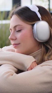 Gülümseyen genç beyaz kadın evde eğleniyor ve müzik dinliyor. Memnuniyet, eğlence ve ferahlama kavramı. Dikey video.