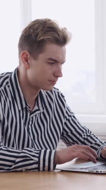 Profesyonel ofis ortamında bir proje üzerinde çalışırken, üretkenliğe ve görevleri geliştirmeye konsantre olarak dizüstü bilgisayarda yazan konsantre bir serbest yazar. Dikey video.