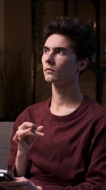 Kafkasyalı genç yetişkin bir adam not defterine fikirler yazıp düşünüyor ya da çizelge hazırlıyor, gece geç saatte kanepede oturuyor. Dikey video.