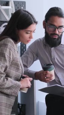 Konsantre olmuş çok uluslu iş arkadaşları belgelerle birlikte çalışıyor, sohbet ediyor ve ofisteki mali durumları analiz ediyorlar. Dikey video.