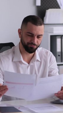 Ofisteki video görüşmesi sırasında evraklarla çalışan orta yaşlı, olumlu bir erkek ofis çalışanı. Uzaktan tartışma ya da sohbet konsepti. Dikey video.