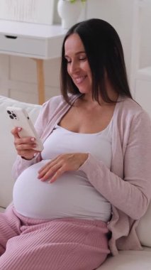 Neşeli orta yaşlı, beyaz hamile kadın evde hobi yaparken internet üzerinden sosyal medyada sohbet ediyor. Dikey video.