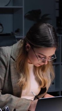 Özenli, beyaz, genç, yetişkin bir ofis çalışanı. Belgeleri inceliyor, ücretleri denetliyor ve akşam ofisinde çalışıyor. Dikey video.