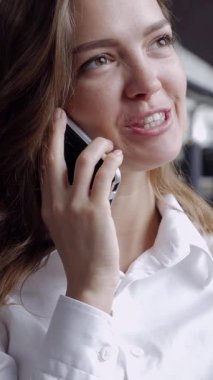 Ofiste çalışırken telefonla konuşan mutlu, beyaz, genç bir ofis çalışanının portresi. Dikey video.