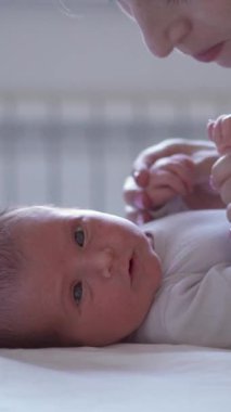 Sevgi dolu ve pozitif beyaz orta yaşlı anne evde yatarken bebeğini öpüyor. Şefkat ve ilgi kavramı. Dikey video.