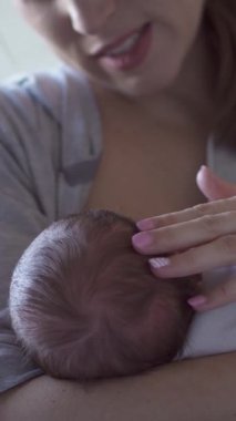 Orta yaşlı, beyaz bir anne, evde küçük bir bebeği emziriyor. Eksiklik, annelik ve beslenme konsepti. Dikey video.