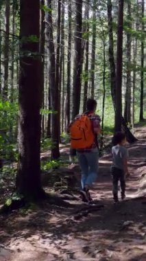 Aktif anne ve okul çocuğu, doğa dolu bir tatil boyunca ormanda gezinip, keşfe çıkıyor, yürüyüş yapıyor ve kaynaşıyor. Dikey video.