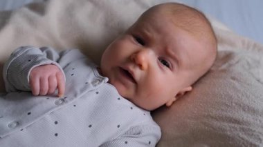 Neşeli bir bebeğin portresi, yeni doğmuş, evde bir yatakta yatıyor. Evcil bir ortamda çocukluk, bebeklik ve erken çocukluk.