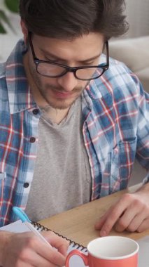 Ciddi bir çalışan, ofiste çalışırken not defterine not alır. Planlama gündemine ve programa odaklanmış, düzenli ve üretken kalıyor. Dikey video.