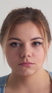 Düşünceli ve odaklanmış bir kadının ciddi ve sert portresi beyaz bir arka planda yoğunluk ve düşünce sergiliyor. Dikey video.