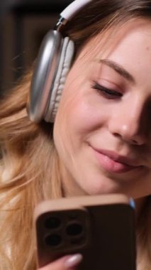 Arkadaş canlısı ve olumlu genç beyaz kadın gece yarısı evde boş vakitlerinde müzik ve cep telefonuyla dinleniyor. Dikey video.