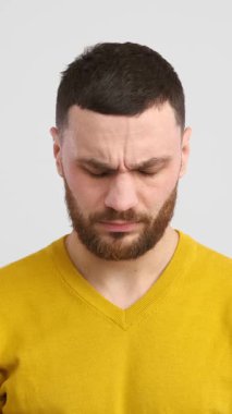 Yorgun ve sağlıksız beyaz bir adam hasta ve beyaz bir arka planda migrenden muzdarip. Sıkıntı ve stres refahı etkiler. Dikey video.