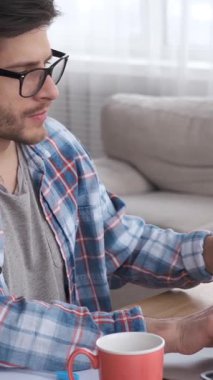 Ciddi bir adam ev ofisinin bilgisayarında çalışırken bir telefona cevap veriyor. Sohbet ve pazarlığa odaklanmış, işini verimli bir şekilde yürütüyor. Dikey video.