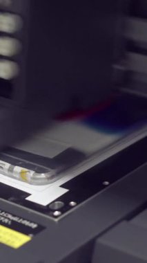 Modern, otomatikleştirilmiş yazıcı, bir telefon kılıfı üzerinde tasarımlar yaratıyor, iş üretiminde gelişmiş teknolojinin altını çiziyor. Yazdırma cihazı konsepti. Dikey video.