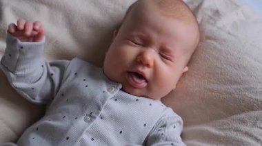 Yatak odasında beşiğinde yatarken bebek hapşırıyor. Bebeklik ve mutluluğun pozitif çocukluk anlarının tadını çıkarıyor..