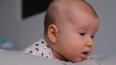 Yeni doğmuş bir çocuğun yakın plan portresi evde yatakta uzanmış, merakla dünyayı keşfediyor. Bebek sıcaklığı, yumuşaklık ve erken ergenlik anları yaşıyor..