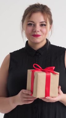 Beyaz arka planda kırmızı kurdeleyle sarılı hediye kutusunu tutan mutlu kadın bayram neşesini ve hediyesini ifade ediyor. Dikey video.